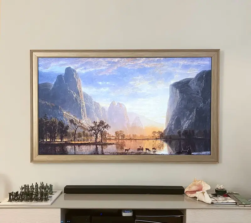 Frame TV with a light wood bezel showing a mountain landscape, mounted above a media console